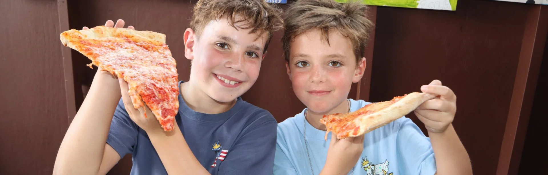 Two Driftwood campers holding up big slices of pizza