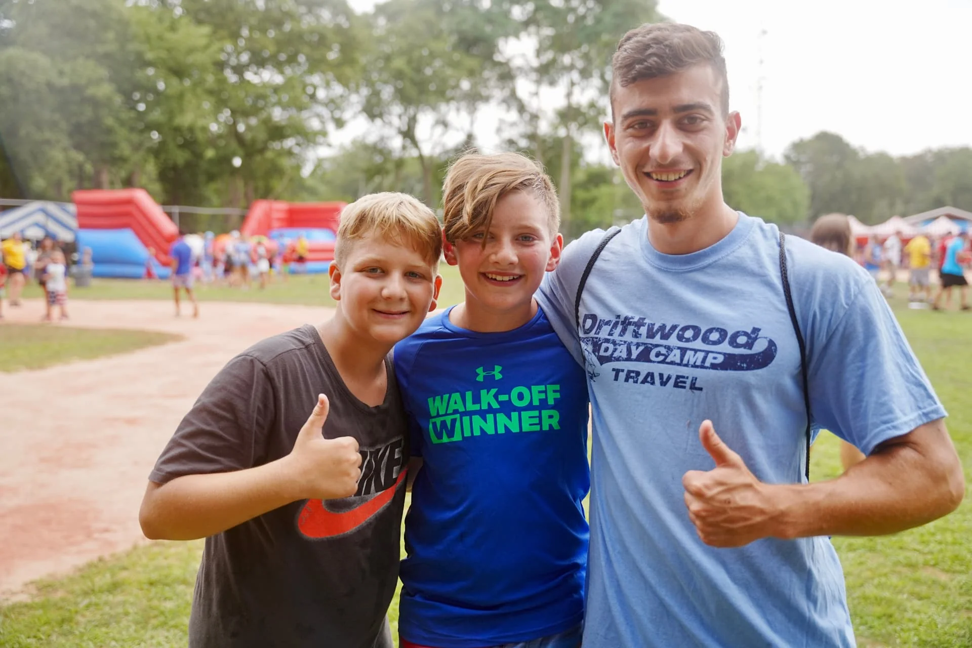 Two Driftwood campers and a staff member smiling with thumbs up on the field
